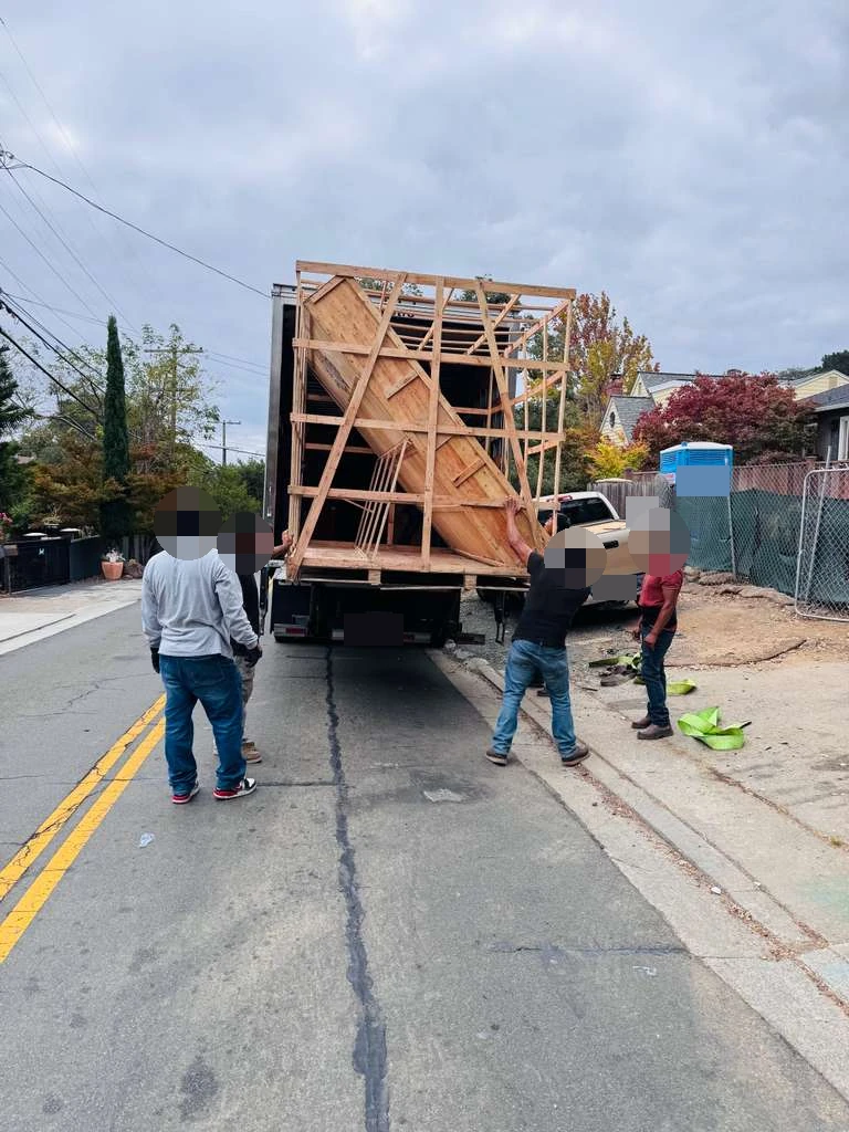 Wooden-framed cargo at the rear of the delivery vehicle during the residential handoff; faces and identifying details obscured