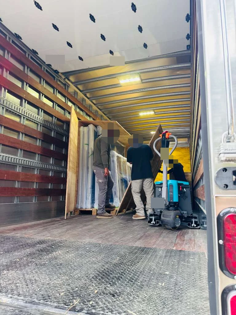 Crated and framed door-and-window cargo inside the delivery vehicle; faces and labels obscured
