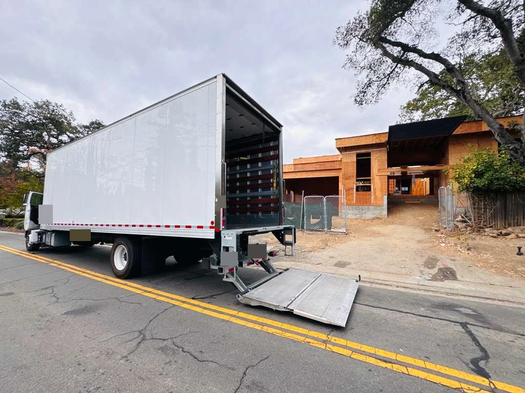 Customer-supplied photograph of the delivery vehicle beside a U.S. home under construction; identifying details obscured
